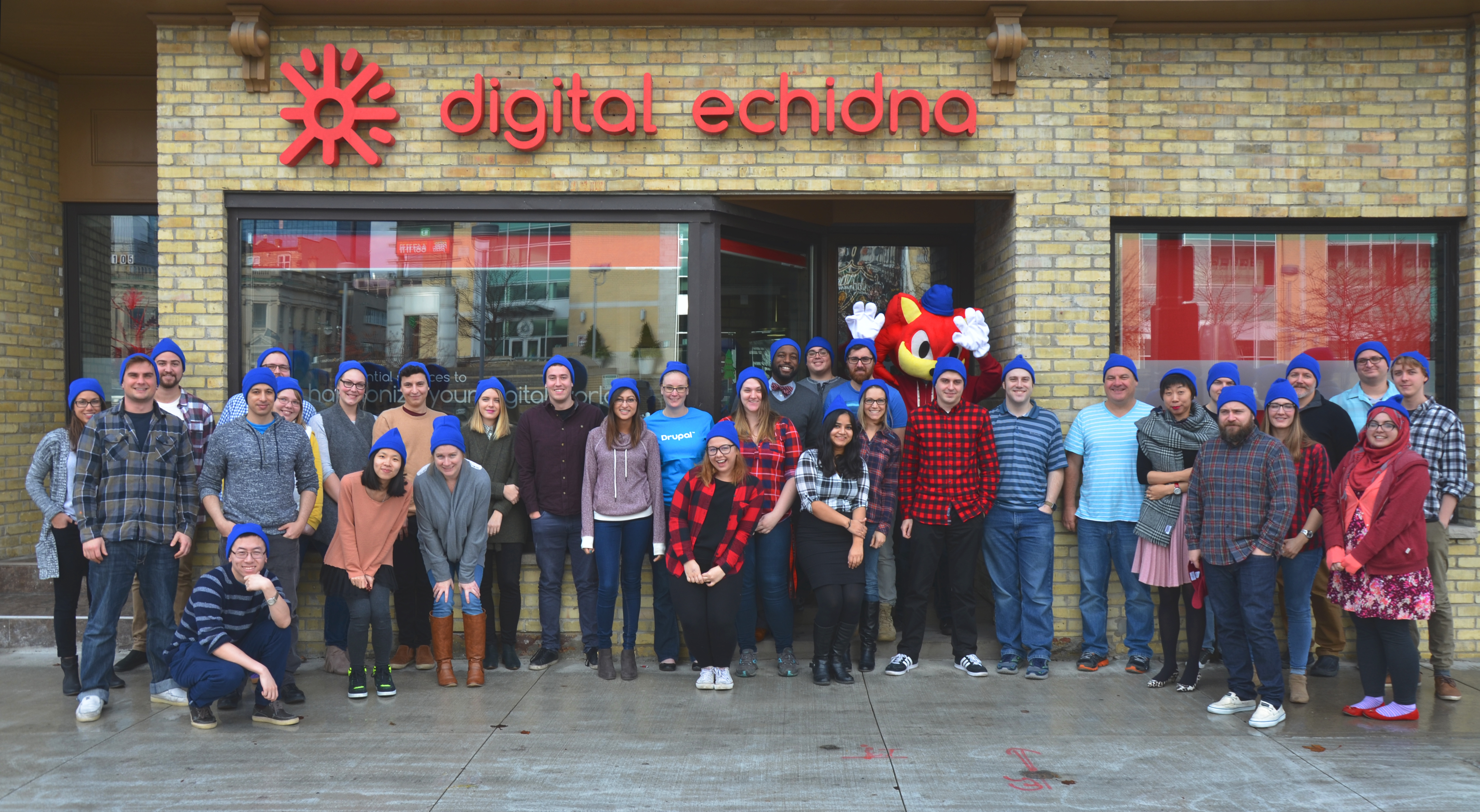 Large group of staff members standing in front of our office on King St. wearing Blue Beanies