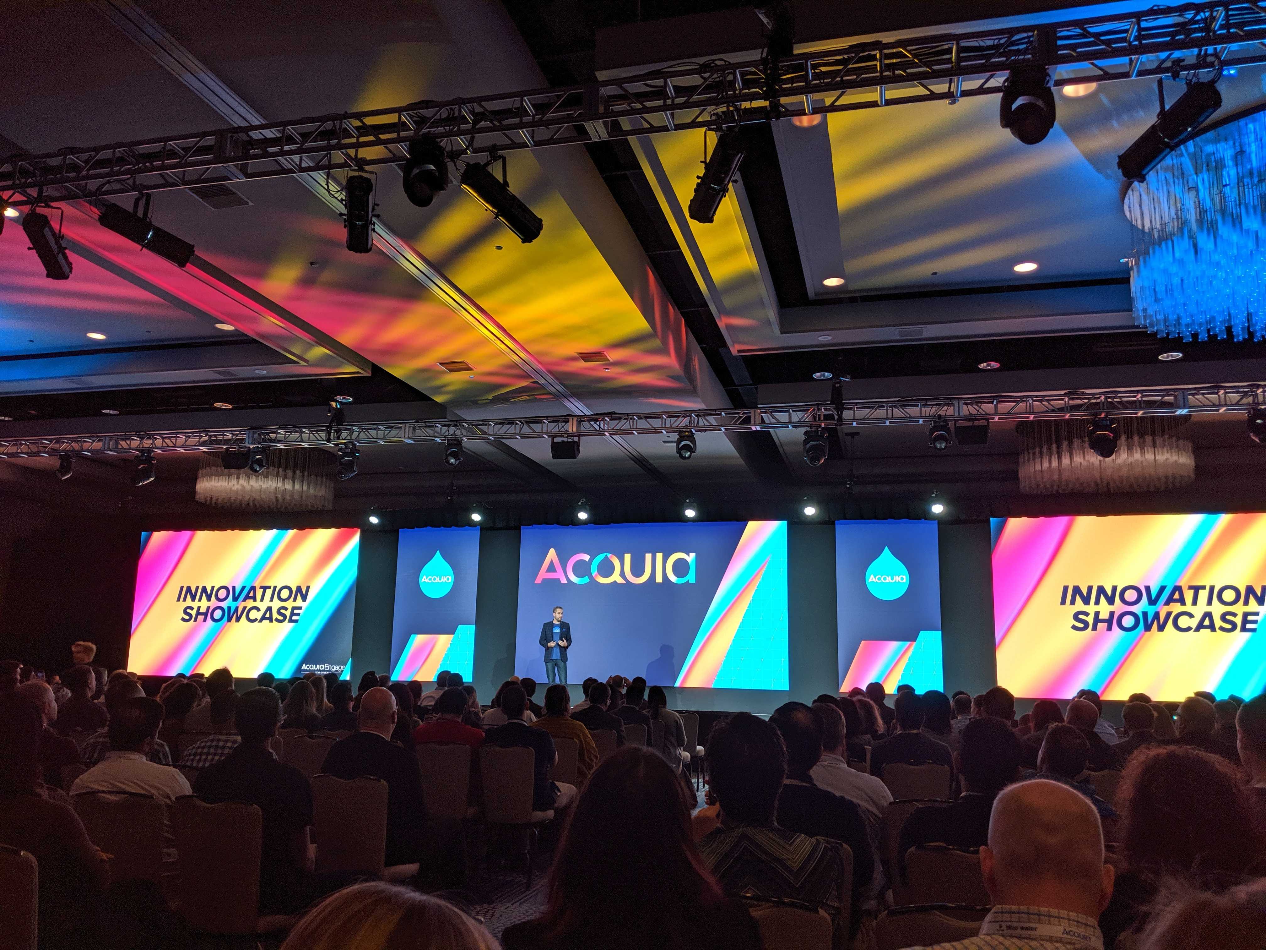 person standing on stage with screens in background, says Acquia Innovation Showcase